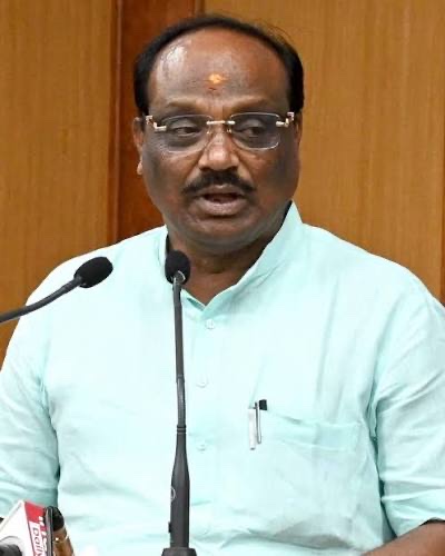 Durga Das Uikey in a pale green kurta, speaking into microphones at a press interaction