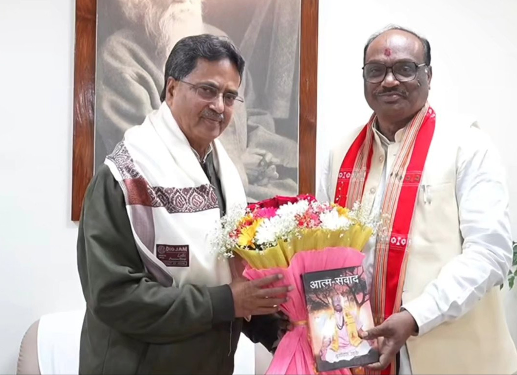 Durga Das Uikey, in a white kurta and red stole, presenting a bouquet and a Hindi book to a dignitary wearing a white shawl