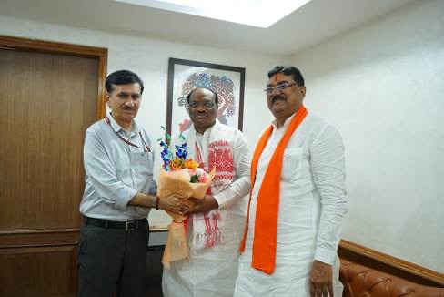 Durga Das Uikey, in a white kurta and stole, receiving a bouquet from an official, with a colleague in a saffron stole beside him