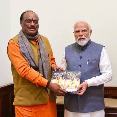 Durga Das Uikey, in a saffron kurta and ochre waistcoat, presenting a book to Prime Minister Narendra Modi
