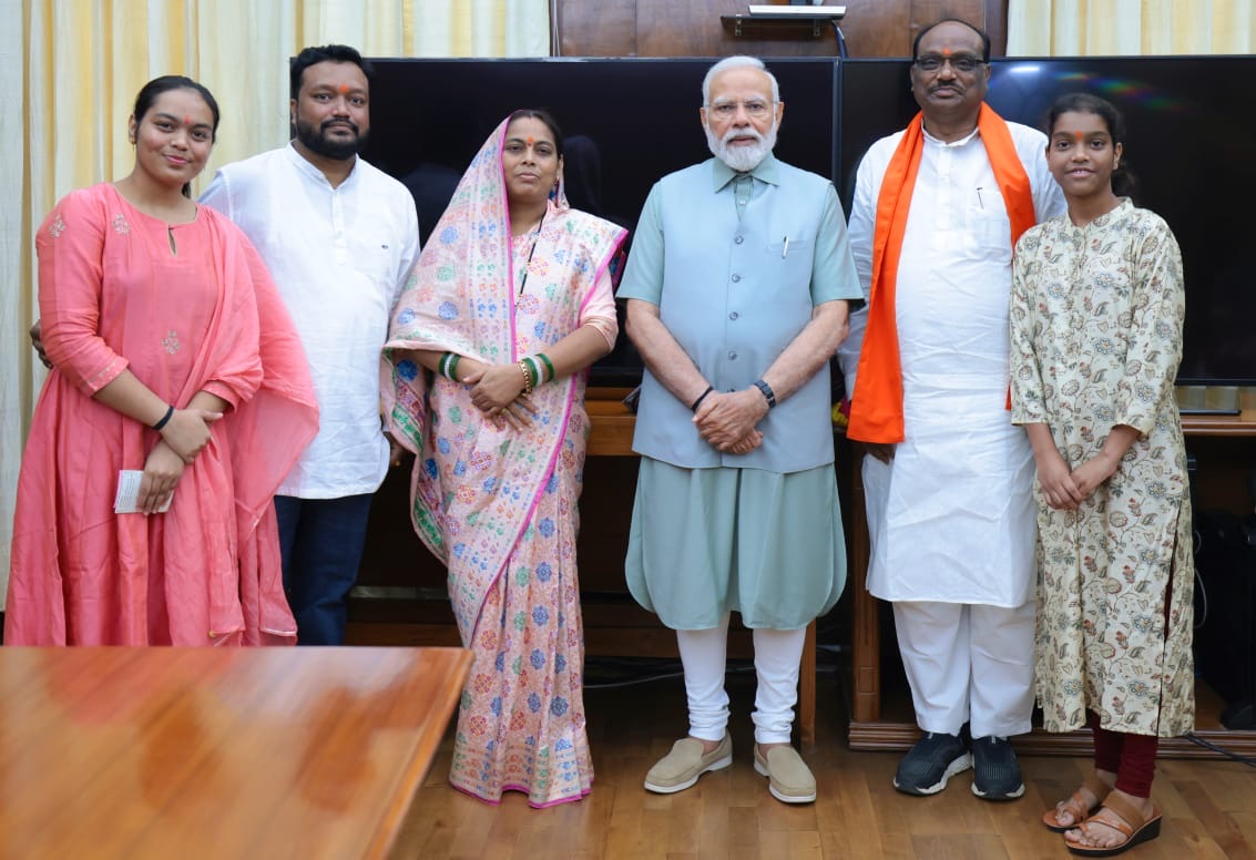 Durga Das Uikey, in a white kurta and saffron stole, standing with Prime Minister Narendra Modi and four guests in an office