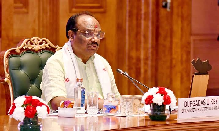 Durga Das Uikey seated at a conference table with a name plate reading Minister of State for Tribal Affairs, chairing a meeting