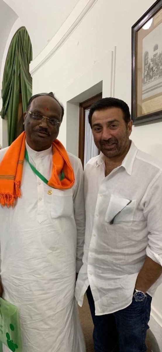 Durga Das Uikey in a white kurta and saffron stole standing beside a fellow Member of Parliament inside Parliament House
