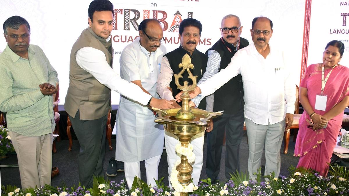 Durga Das Uikey and other dignitaries lighting a tall brass lamp on stage beneath a banner for the National Conclave on Tribal Languages and Museums
